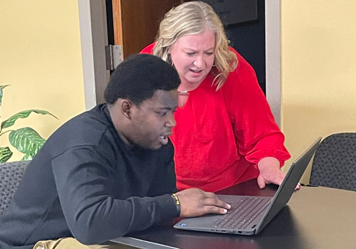 Woman helping young man search for job opportunities on the computer.
